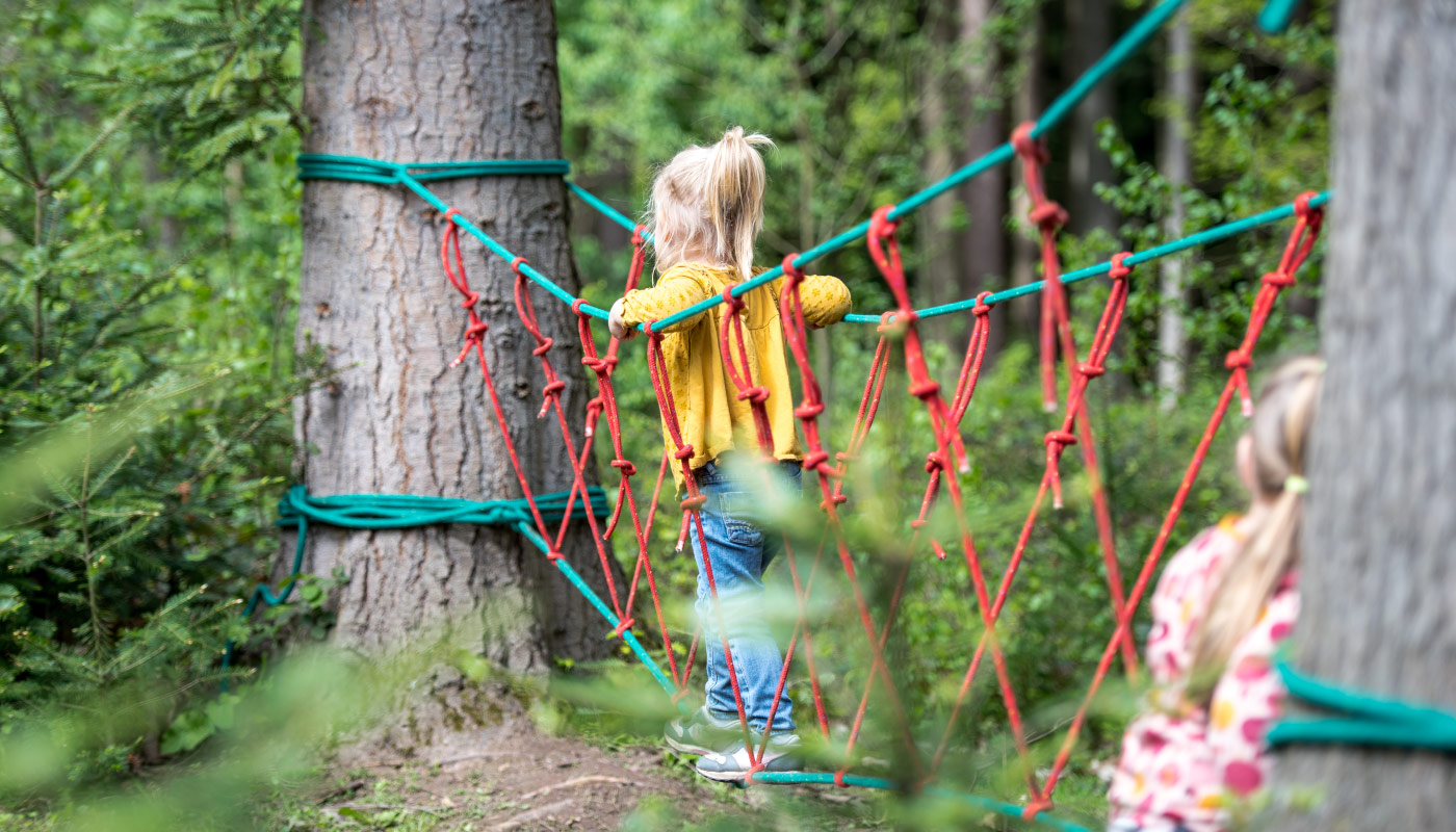 Kinder auf einem roten Kletterseil im Wald beim Spielen