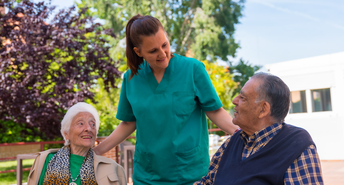 Pflegekraft im Gespräch mit zwei älteren Menschen im Garten.
